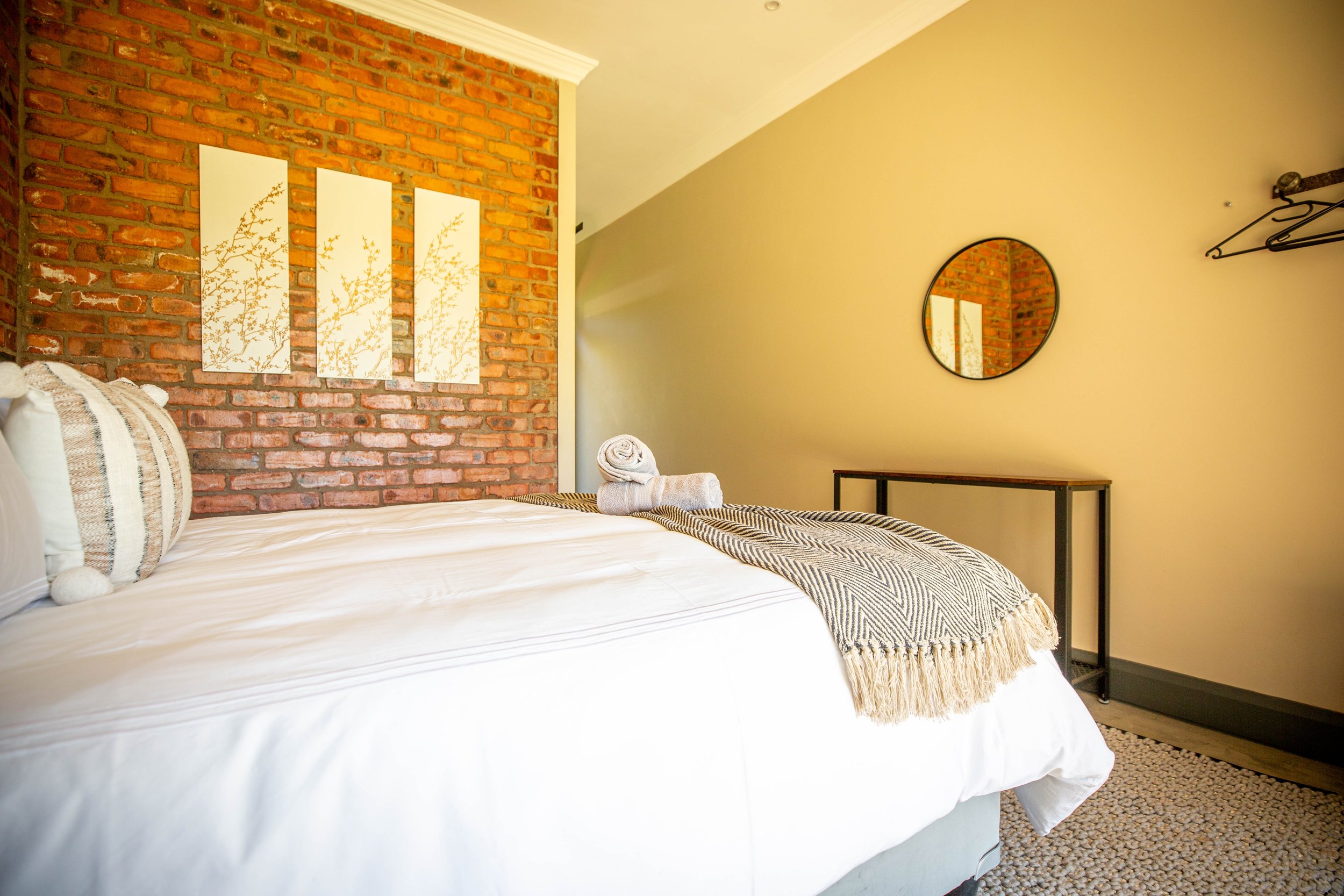 Queen bed with botanical prints on the brick wall in Annex Room 3